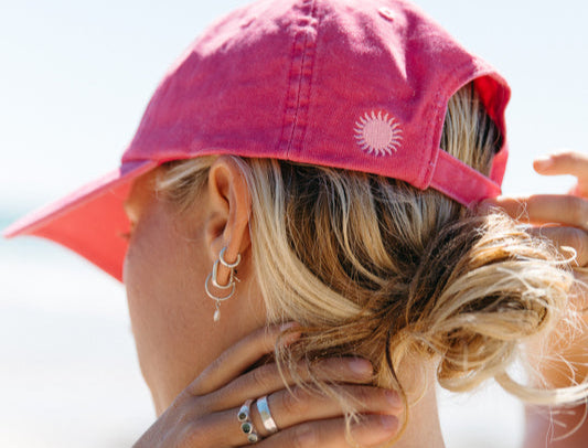 Person wearing a Sol Sista Collective cap with a sun logo, standing outdoors.